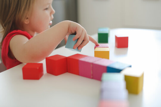  child playing and building with colorful wooden toy bricks on white wooden table. Early learning and development