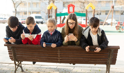 Group of boys and girls addicted in their phones spending time together outdoors