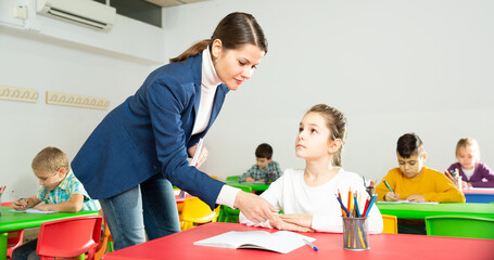 Female teacher helps schoolgirl complete an assignment in an elementary school class. High quality...