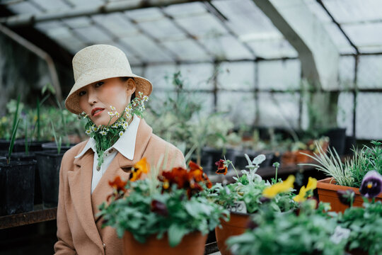 Portrait of asian girl in white cap and gypsophila flowers under her collar	sits in greenhouse 