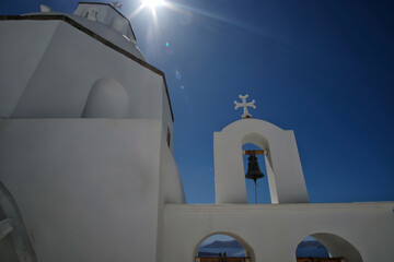 Angle view of a whitewashed church with a bell, a crucifix and sunstars in Santorini 