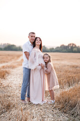 Fototapeta na wymiar Young pregnant woman with her daughter and husband, happy family hugging on a golden field in the countryside. Family relations. Future parents