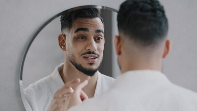 Funny arabian indian bearded man speaking to reflection looking in bathroom mirror. Smiling sexy millennial guy narcissist speaks to himself rehearses speech performance oratory affirmation in morning