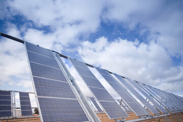 Obraz premium Solaranlage mit mehreren Reihen von Kollektoren zur Gewinnung von Strom. Blauer Himmel mit Sonne und Wolken 