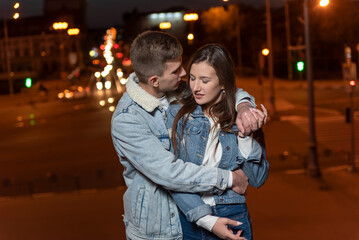 Fototapeta premium Guy gently hugs his girlfriend on evening city background. Relationship outdoors