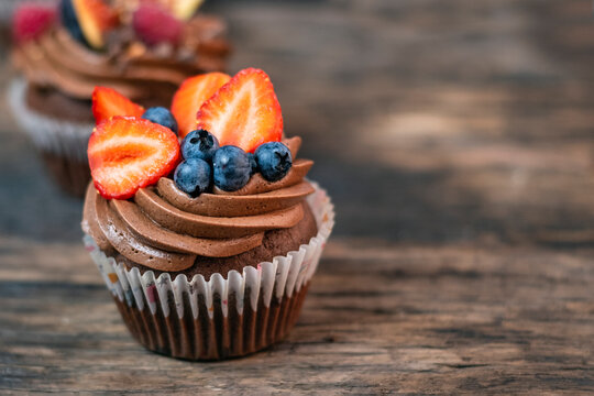 Chocolate mafin with butter cream is decorated with blueberries and strawberry pieces. Beautiful close-up cake on wooden table