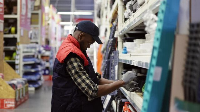 Male supervisor arrange goods on shelves of hardware store, side view
