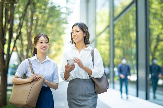 スマートフォンを持ってビジネス街を歩くビジネスウーマン2人