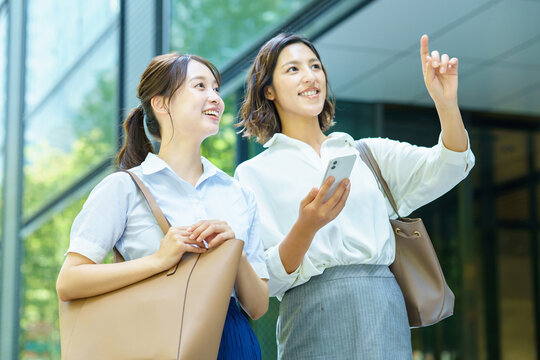 スマートフォンを持ってビジネス街を歩くビジネスウーマン2人