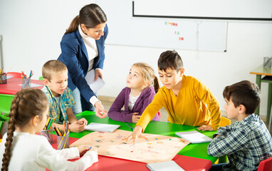 Teacher and happy children sitting at table with board game and dice in school. High quality photo