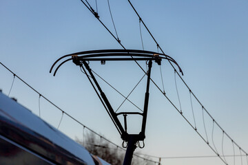 Pantograph of a tram connecting on electric line with blue sky as background, Electric railway train and power supply lines, Cables connections and metal pole overhead catenary wire.