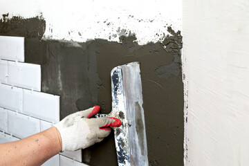 Wall cladding with ceramic tiles. The worker aligns the glue on the wall with a spatula. The stage...