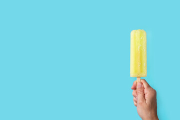 Hand holding a lemon popsicle on blue background. Copy space