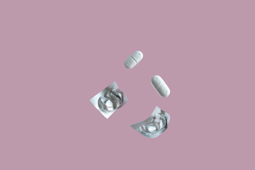 
medical composition. levitation of two tablets and two blisters from packaging on a pink background.