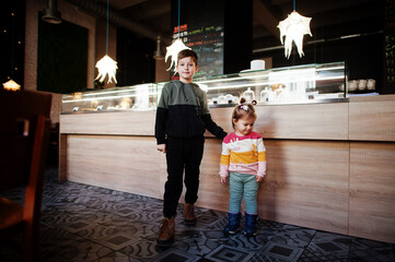 Brother with sister in cafe choose a dessert from shop window.