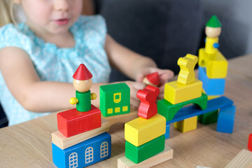 close-up of children's educational toys in hands of toddler, small child, a 2-year-old girl builds houses for characters from color blocks, concept of childhood, earlier child development, creativity