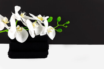 Black spa setting with black towels, white orchids on the black background. Spa concept, copy space