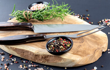 Wooden Cutting board, spice and rosemary with fork and knife for meat on black background - Powered by Adobe