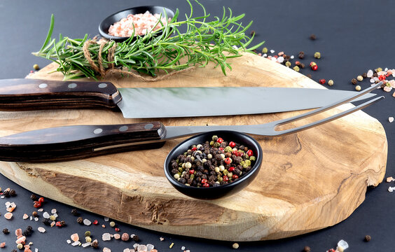 Wooden Cutting board, spice and rosemary with fork and knife for meat on black background
