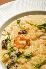 Appetizing risotto with seafood (shrimp and mussel) garnished with microgreens (pea sprouts) in a beautiful white plate.