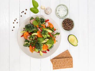 vegetable salad in a white plate on a white wooden background.