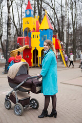 Stylish mom with stroller  walking on   playground  in   spring
