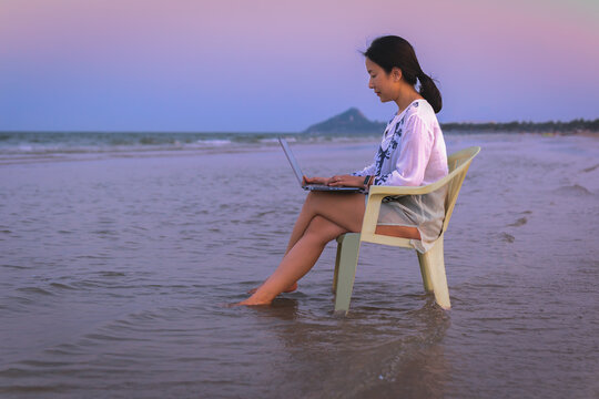 Side view businesswoman using laptop while sitting in a chaie on the beach.