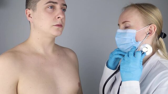 Auscultation. The therapist listens to the patient lungs. The man complains of coughing and difficulty breathing. A doctor in a gown, mask and with a phonendoscope examines a patient.