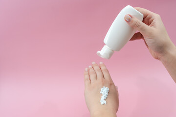 Female hands squeezing cream from tube on pink background. Сosmetic bottles for beauty or medicine products