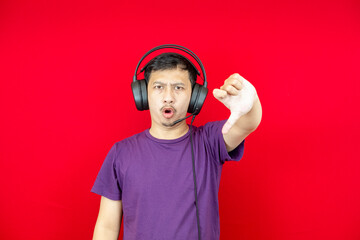 Asian man wearing headset dissatisfied and displeased with showing disapproval sign, disagree symbol, giving thumbs down.