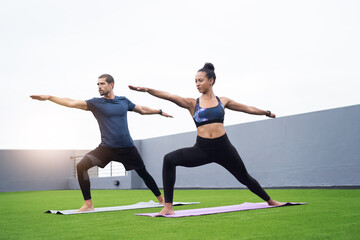 Fototapeta premium Maintaining balance and form is key. Shot of a young man and woman practising yoga together outdoors.