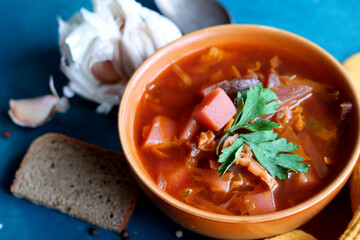 Traditional Ukrainian soup Borscht. Close up photo of soup bowl, wooden board, spoon, bread and spices on a table.  Deep blue background with copy space. 