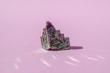 Synthetic bismuth Bismuthumcrystal with iridescent oxide film on pink background close up isolated....
