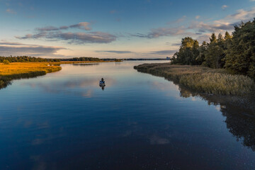 Tranquil aerial view of two fishermen fishing from a boat at sunset on a river in Northern Europe. On the right of the scene is a forest reflecting on the water and on the left is a layer of low