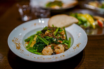 からすみを散らした白い皿に盛られた菜と小エビのアンチョビオイルソースパスタ