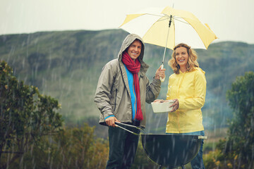 Come rain or shine. Shot of a couple happily barbecuing in the rain.