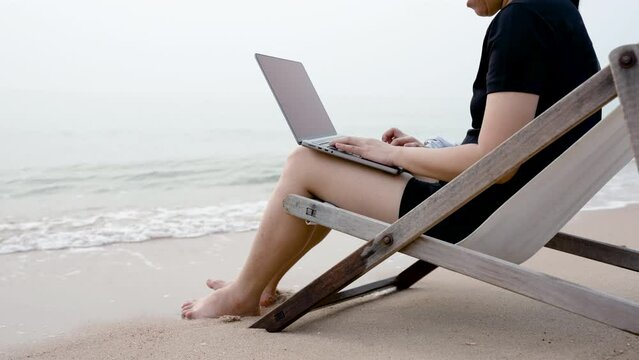 4K 50fps, on vacation you have to do your work too. Half-body pictured below Close Up Asian woman sitting on a beach chair using his Notebook laptop to work on his morning break at the beach.
