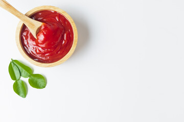 Top view tomato ketchup in a wooden cup placed with green leaves copy space isolated on a white background.