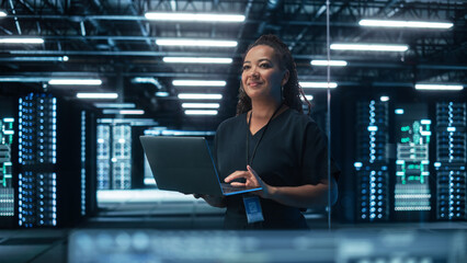 Portrait of Multiracial Mature Female IT Specialist Using Laptop, Standing in Data Center....