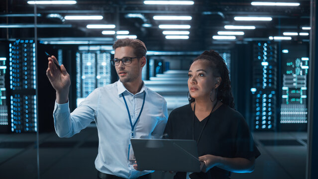 Entrepreneur and IT Specialist Talk and Look at the Laptop in Diverse Big Data Center Server. Technical Support Scientist works with Cloud Infrastructure Architect. 