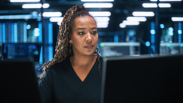 Focused IT Specialist Working on Computer in Office Environment. Diverse Multiethnic Female Developer is Using Two Monitors while Writing Code Late at the Night