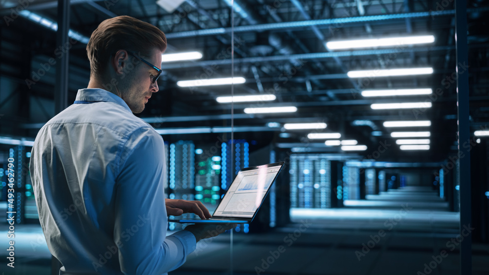 Poster back view of male specialist using laptop in big data center office. high speed data transfer, serve