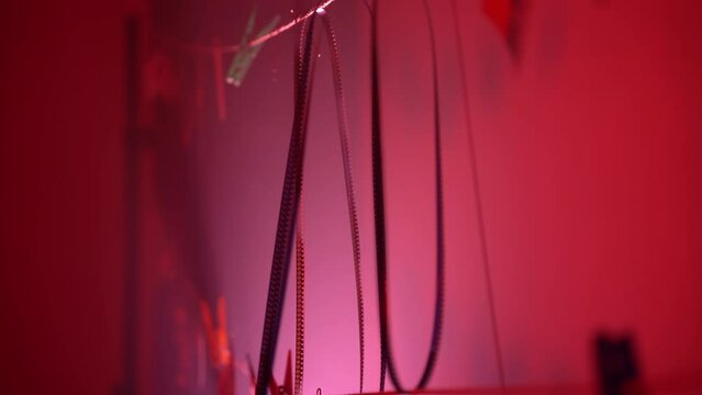 Cinematography and developing archival film reels in work studio with red illumination, retro bobbin pellicles hanging on rope being ready for projecting. Vintage film reel tapes developing