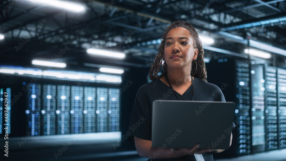 Poster female mature multiracial e-business entrepreneur look away and holding laptop at data center server