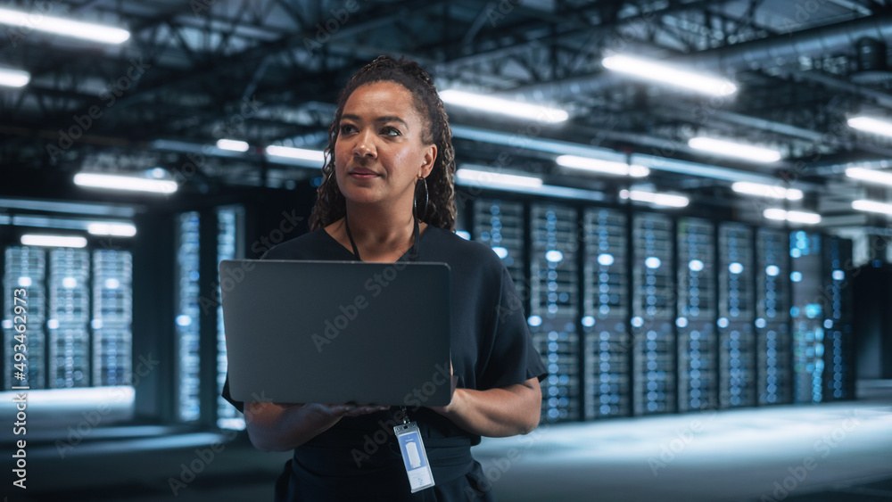 Poster Portrait of Successful African American Female IT Specialist Using Laptop, Standing in Data Center. System Administrator Works on Web Services. Cloud Computing, Server Analytics, Cyber Security