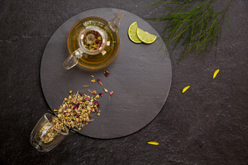 herbal tea in teapot and lemon on black background