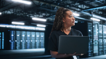 Mixed RaceFemale IT Specialist Uses Laptop Computer in Data Center. Server Farm Cloud Computing Facility with Maintenance Administrator Working. Cyber Security Engineer Working in Network Protection