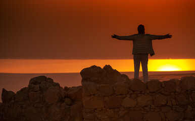 Woman is meeting a sunrise on the top of old wall, she turned her hands to the sun