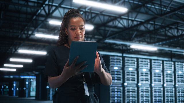 Successful Female IT Specialist Using Laptop Computer, while Standing at Big Warehouse Data Center. System Administrator working with Computing SAAS, Cloud Services. E-Business Digital Entrepreneur