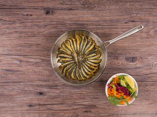 traditional fish skillet and salad on wooden table